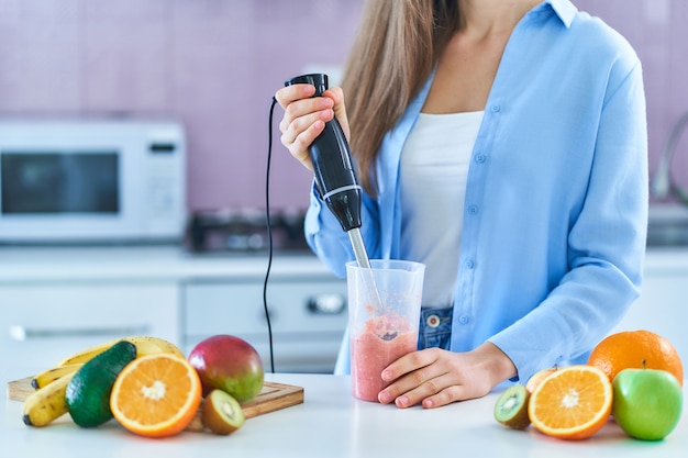 Het wijfje gebruikt handmixer om vers fruit te mengen om dieet smoothie thuis in de keuken voor te bereiden