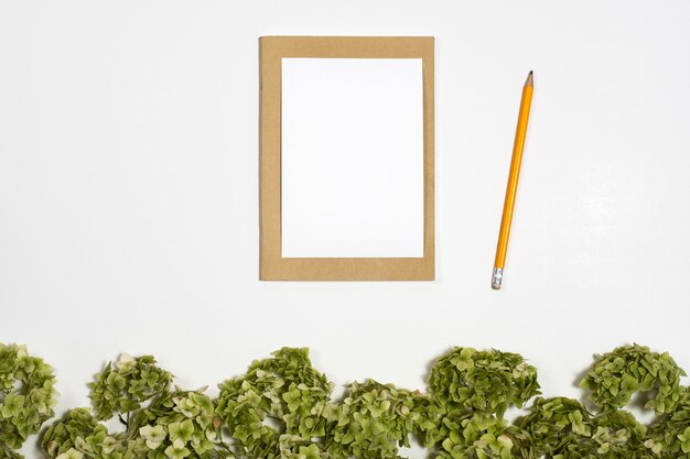 Het witte blad onder op notitieboekje naast een potlood ligt op een achtergrond met een groene tak