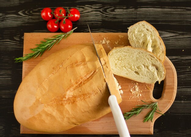 Het witte brood wordt gesneden met een mes op een houten raad met kersentomaten en rozemarijn