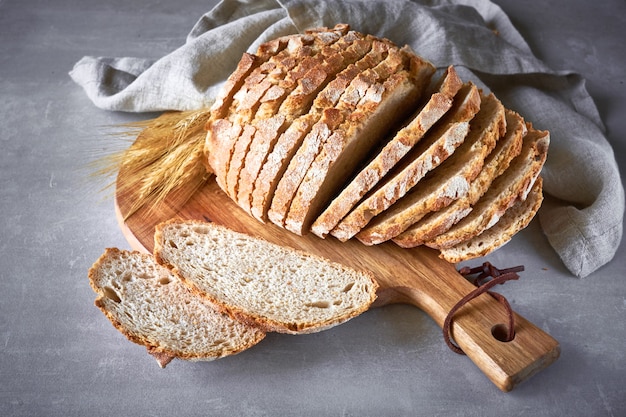 Het witte ronde brood van Slliced met tarweoren op houten scherpe raad op grijze steen