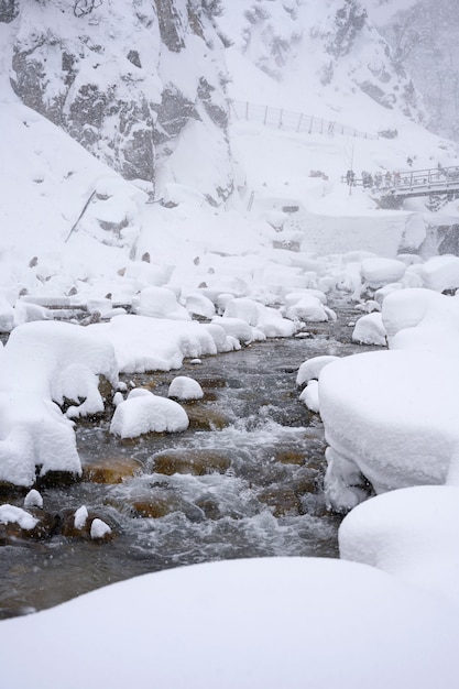 Foto het witte sneeuwen behandelde de berg en stenen op bevriezende rivier met sneeuwapen die onder de achtergrond van de sneeuwonweer over hemelwintertijd zitten, japan