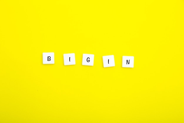 Het woord begin is geschreven in letters op kleine witte vierkantjes op een gele achtergrond