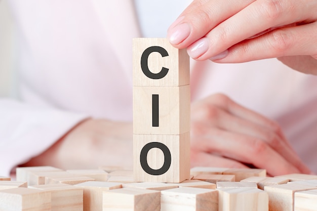 Het woord CIO op een houten stuk speelgoed blokken met de handen van de vrouw, roze achtergrond. Bedrijfsconcept. CIO - afkorting van Chief Information Investment Officer