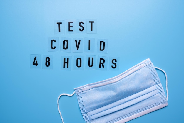 Het woord Covid test 48 uur op een blauwe achtergrond en een medisch masker.