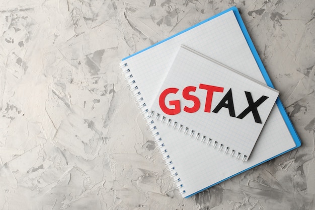 Het woord gst tax met een notitieblok op een lichte betonnen achtergrond. bovenaanzicht met ruimte voor tekst