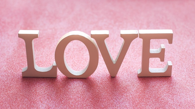 Foto het woord love is gemaakt van witte letters op een roze glitterachtergrond valentijnsdag liefde zachte boke