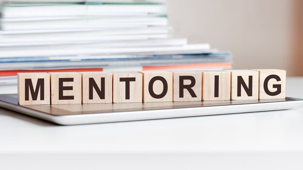 Het woord mentoring is geschreven op houten kubussen die op een notitieblok staan. Kan worden gebruikt voor zaken, onderwijs, financieel concept.