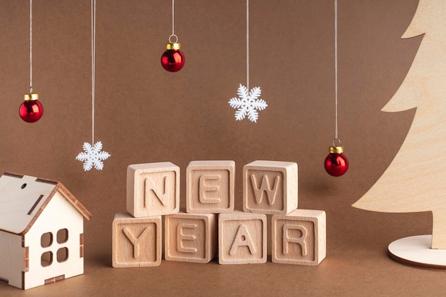 Het woord nieuwjaar samengesteld uit houten kubussen op een bruine achtergrond Houten huis kerstboom en andere kerstversieringen Kerstkaart