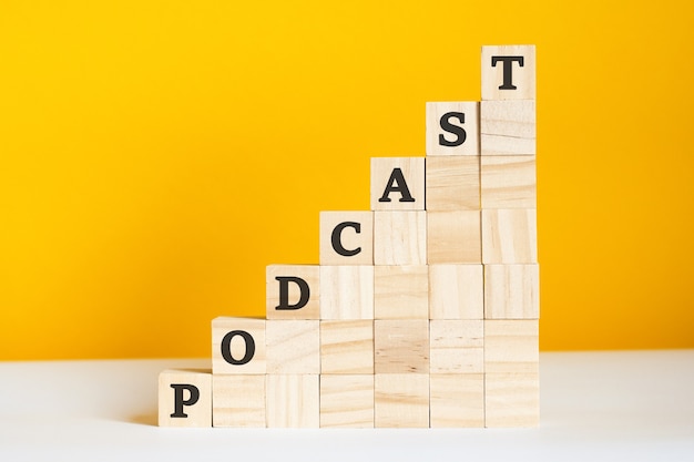 Het woord PODCAST is geschreven op een houten kubus. blokken op een felgele achtergrond. bedrijfshiërarchieconcept en marketing op meerdere niveaus. selectieve focus