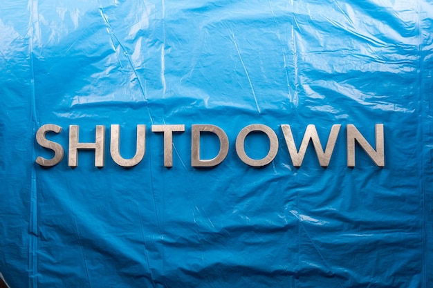 Het woord shutdown gelegd met zilveren metalen letters op een verfrommelde blauwe plastic filmachtergrond in plat perspectief