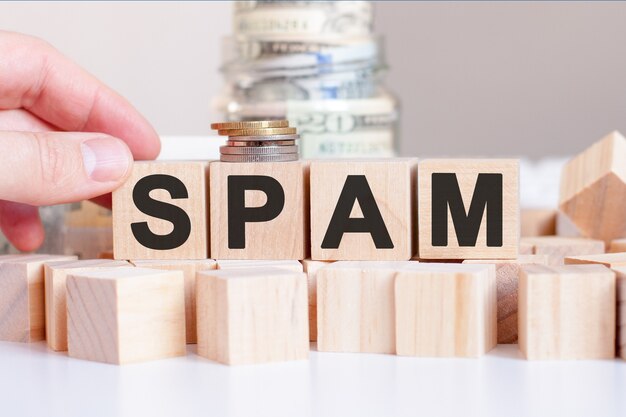 Het woord spam op de houten blokken en een bank met geld achter, bedrijfsconcept