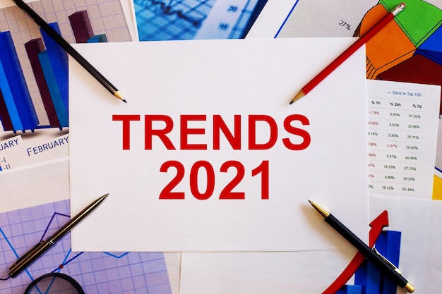 Foto het woord trends 2021 is geschreven op een witte achtergrond in de buurt van gekleurde grafieken, pennen en potloden. bedrijfsconcept