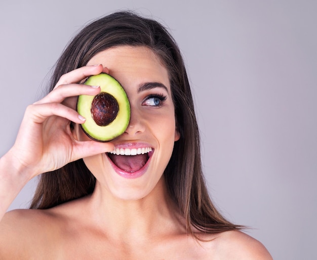 Het zal je huid helpen stralen Studio-opname van een aantrekkelijke jonge vrouw die haar oog bedekt met een avocado tegen een paarse achtergrond