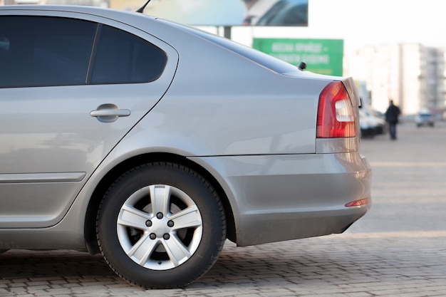 Het zijaanzicht van zilveren auto parkeerde op bedekt parkeerterreingebied op de vage achtergrond van de voorstadweg op heldere zonnige dag. Transport- en parkeerconcept