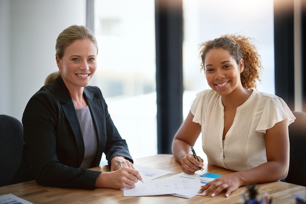 Het zijn verhuizers en shakers op kantoor Portret van twee glimlachende zakenvrouwen die samen aan een tafel in een kantoor zitten