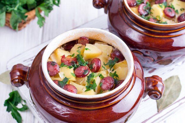 Hete aardappelgoulash met spek en worstjes geserveerd in een keramische kom
