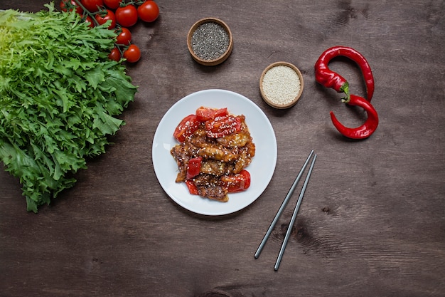 Hete aubergine en tomatensalade in Koreaanse stijl met sesamzaadjes en kruiden. Aziatisch eten. Vegetarisch gerecht. Hout