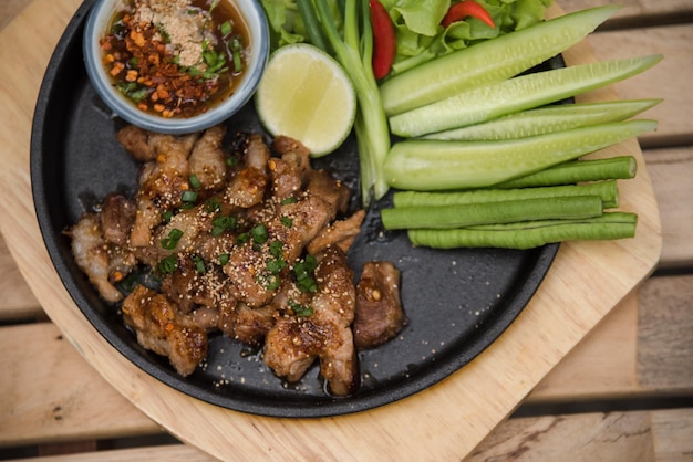 Hete en pittige gegrilde varkenssalade (Nam tok moo) op de houten tafel