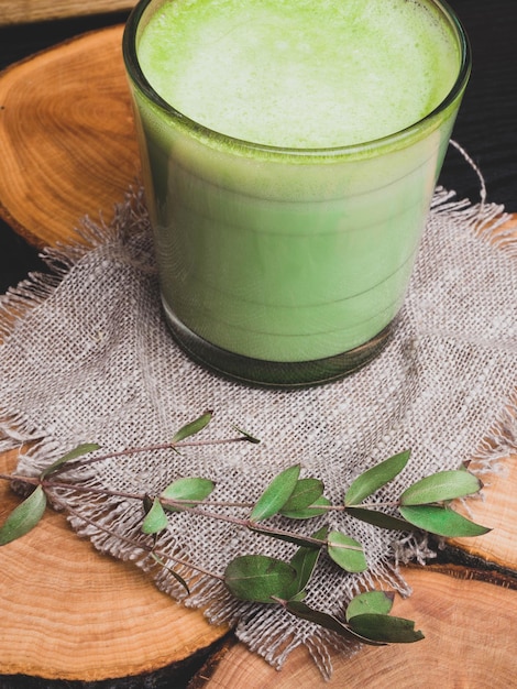 Hete groene thee latte met groene bladeren op jute en houten ondergrond