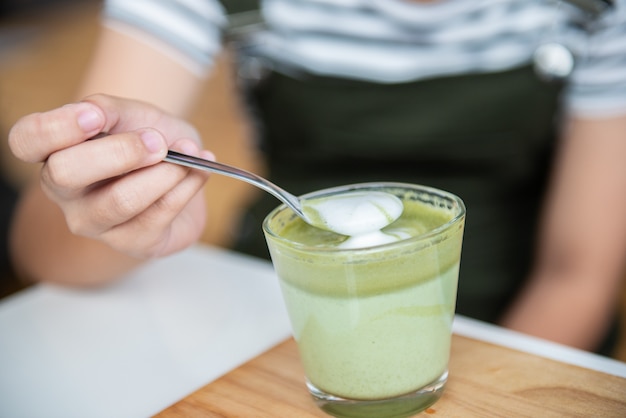 Hete groene thee latte met lepel op houten plaat