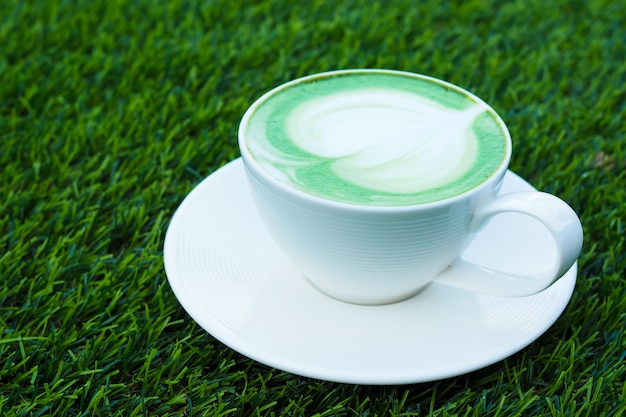 Hete groene theematcha latte in witte kop op groene grasachtergrond