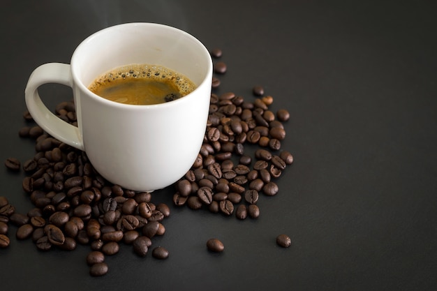 Hete koffie in wit keramisch glas en koffiebonen op de zwarte tafel.