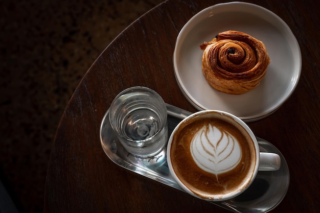 Hete koffie latte met latte art melkschuim in bekermok en Homemade Raisin Deense witte plaat op houten bureau bovenaanzicht Als ontbijt In een coffeeshop in het café tijdens zakelijk werk