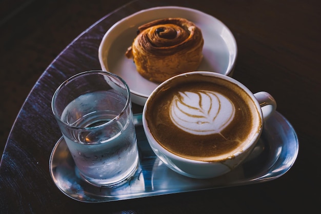 Hete koffie latte met latte art melkschuim in bekermok en Homemade Raisin Deense witte plaat op houten bureau bovenaanzicht Als ontbijt In een coffeeshop in het café tijdens zakelijk werk