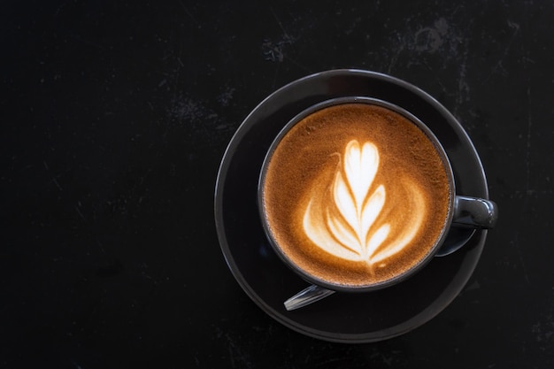 Hete koffie latte met latte art melkschuim in bekermok op zwart houten bureau op bovenaanzicht als ontbijt in een coffeeshop in het café tijdens zakelijk werkconcept