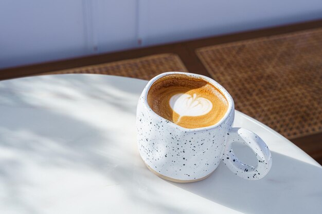 Hete koffie latte met latte art melkschuim in mok met witte stenen patroon op houten bureau op bovenaanzicht Als ontbijt In een coffeeshop in het café tijdens zakelijk werkconcept