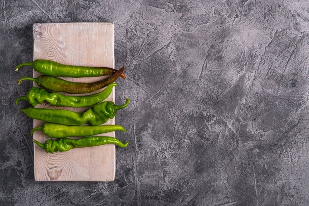 Hete pittige groene chilipepers op houten snijplank, stenen betonnen tafel, kopie ruimte bovenaanzicht