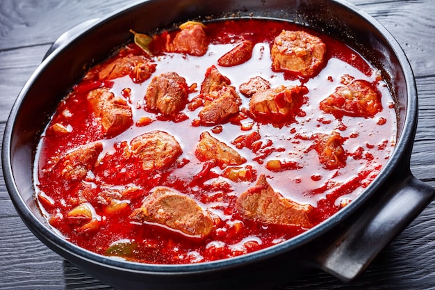 Hete rode Chili en varkensstoofpot of Carne Adobada in een Nederlandse oven op een zwarte houten tafel, Mexicaanse keuken, horizontale weergave van bovenaf, close-up