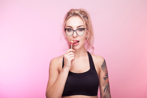 Hete sexy vrouw die een lolly op roze achtergrond likt