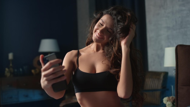 Hete vrouw die selfie mobiele telefoon in slaapkamer neemt Meisje dat pret met telefoonbed heeft