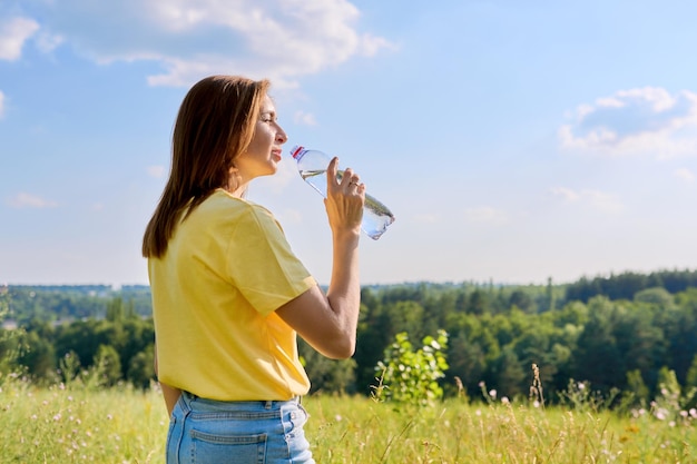 Hete zonnige zomer dorstige volwassen vrouw drinkwater uit de fles voor ons in de natuur