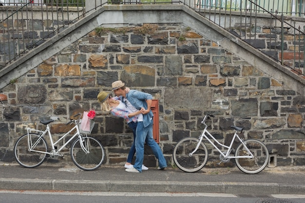 Foto heup jong paar die door bakstenen muur met hun fietsen dansen