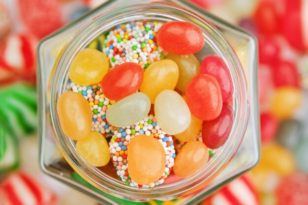 Photo hexagonal jar full of jelly candies with scattered sweets in the background