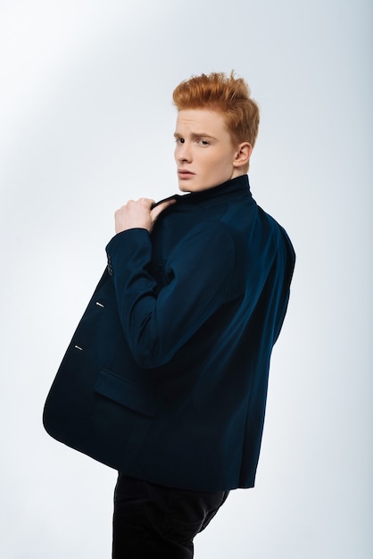 Hey. Handsome determined red-haired young man wearing a jacket and looking over his shoulder and touching his jacket