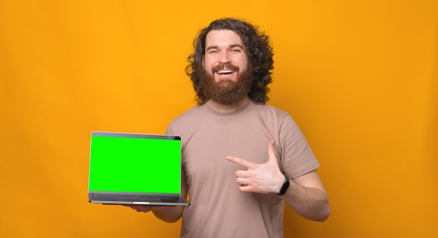 Ehi, guarda questo, uomo barbuto sorridente gioioso con i capelli ricci che punta al laptop con schermo verde