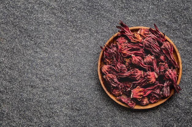 Hibiscus dried flowers in wooden bowl on black background.