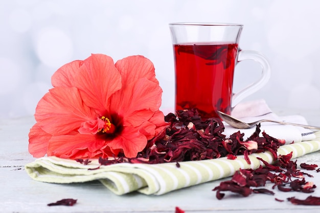 Hibiscus tea and flower on color napkin on wooden table on light background