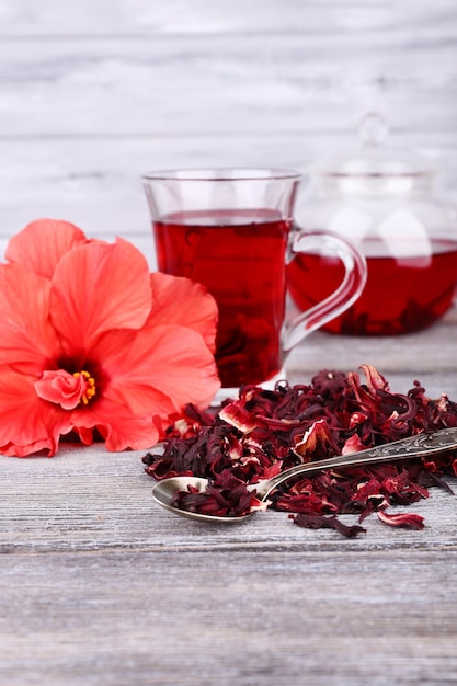 Hibiscus tea in glass teapot and flower on color napkin on wooden background