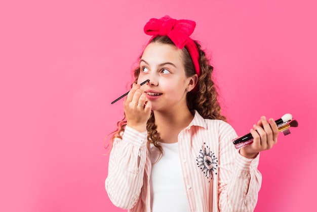 Foto nascondi le imperfezioni ragazza felice con fascia per capelli tieni i pennelli per il trucco concetto di trucco fard o ombretti tono perfetto salone di bellezza moda per adolescenti applicare cosmetici cosmetici per pelle giovane