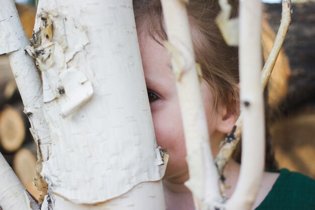 Foto nascondino scena rustica rurale con bambina carina dietro un albero di betulla.