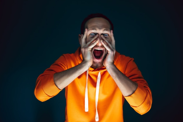 Hiding face. portrait of crazy scared and shocked caucasian man\
isolated on dark background. copyspace for ad. bright facial\
expression, human emotions concept. watching horror on tv,\
cinema.