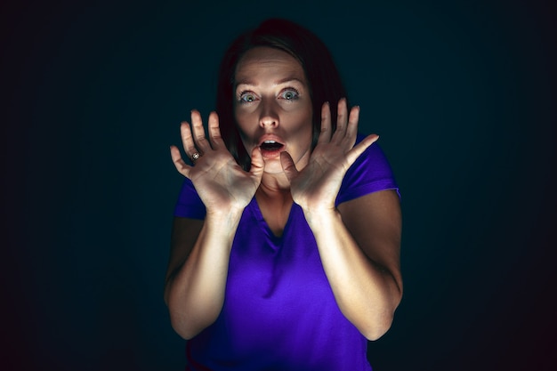 Hiding. Portrait of young crazy scared and shocked caucasian woman isolated on dark background. Copyspace for ad. Bright facial expression, human emotions concept. Looking horror on TV, cinema.