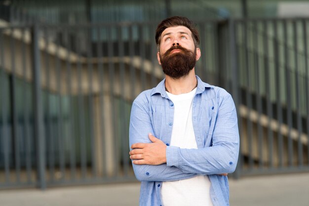 Hier en nu Waar hij aan denkt Peinzende hipster die prettige gedachten denkt Man bebaarde hipster stedelijke achtergrond Regelmatige wandeling in het stadscentrum Zelfverzekerde hipster staat alleen op straat