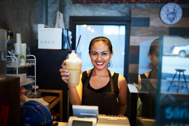 Hier is je bestelling Portret van een jonge barista die een gekoelde koffiedrank omhoog houdt in een coffeeshop