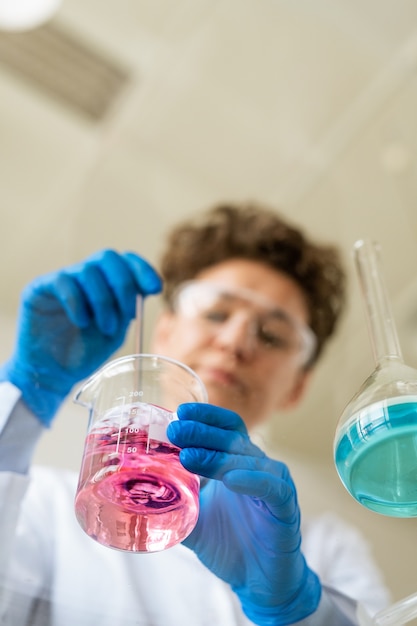 Hieronder weergave van chemicus in beschermende handschoenen reagentia roeren in het bekerglas tijdens de voorbereiding op experiment