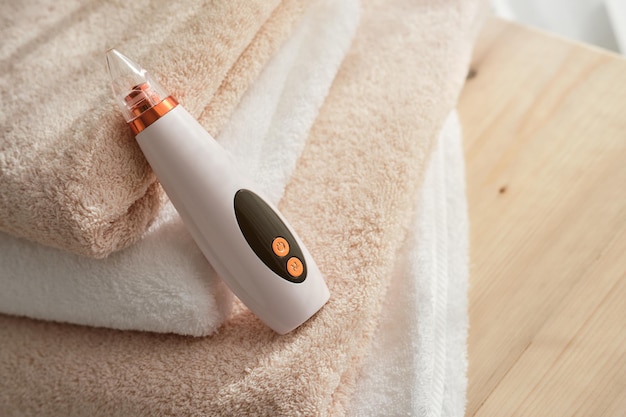 High angle of blackhead vacuum cleaner placed on pile of towels on wooden table in light room at home